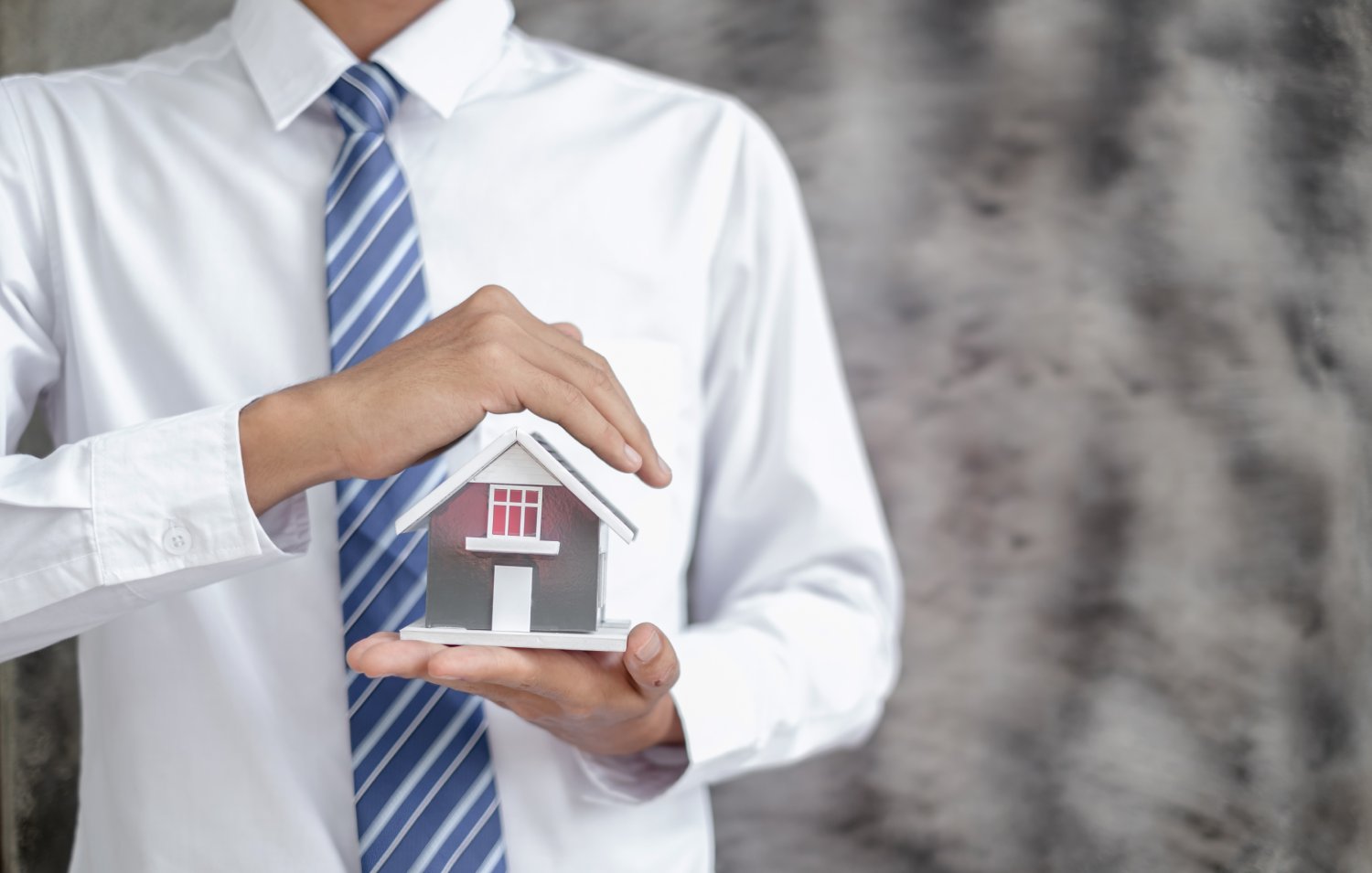 Home insurance concept and real estate. The hand Businessman holding a house model working in investment about renting a house, buying a house, and home insurance.